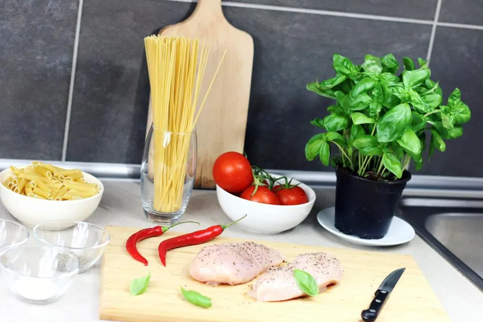 Encimera con albahaca, pasta, tomates y verduras para cocinar